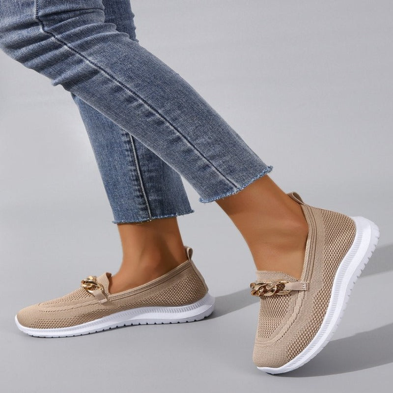 Weiße Damen-Slip-On-Sneaker mit goldener Gliederkette, atmungsaktivem Strickmaterial und weißer Sohle, kombiniert mit blauen Jeans