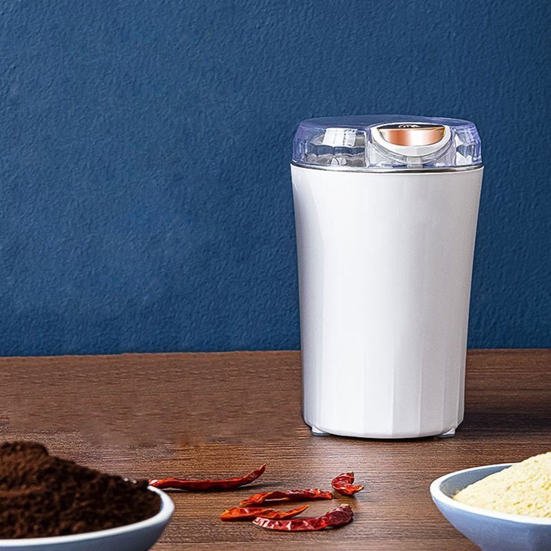 Elektrische Kaffeemühle in Weiß auf Holztisch, umgeben von gemahlenem Kaffee, getrockneten Chilischoten und gelbem Pulver