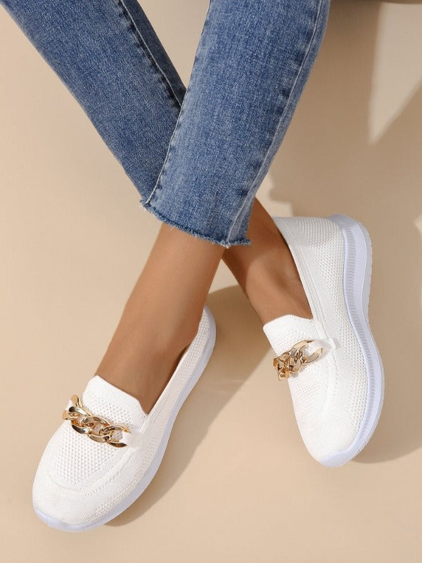 Weiße Damen-Slip-On-Sneaker mit goldener Gliederkette, atmungsaktivem Strickmaterial und weißer Sohle, kombiniert mit blauen Jeans